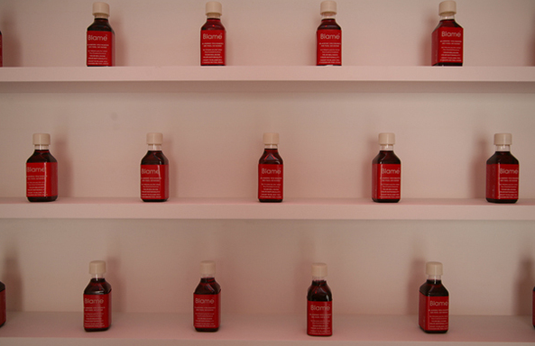 Shilpa Gupta, Blame, 600 bottles filled with simulated blood presented on shelves and red light