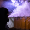 Man sitting in dark room with purple light blowing vape smoke